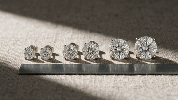 Three pairs of diamond solitaire studs laid out by size against a steel ruler