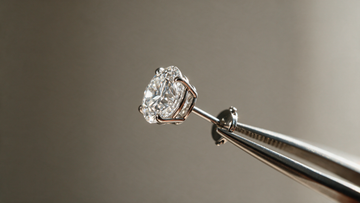 A single diamond solitaire stud held in jeweller's tweezers with light raking across the facets
