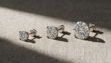 Three pairs of diamond solitaire studs arranged in ascending size on linen