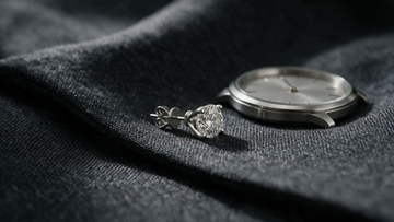 A single men's diamond stud on charcoal wool suiting beside a steel watch
