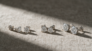 Three pairs of diamond solitaire studs laid out for comparison on linen