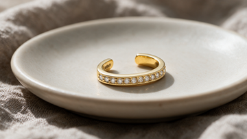 A diamond ear cuff resting alone on a bone-white ceramic dish
