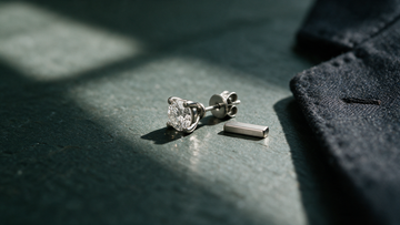 Men's platinum diamond solitaire stud on dark slate, platinum vs 18K white gold comparison