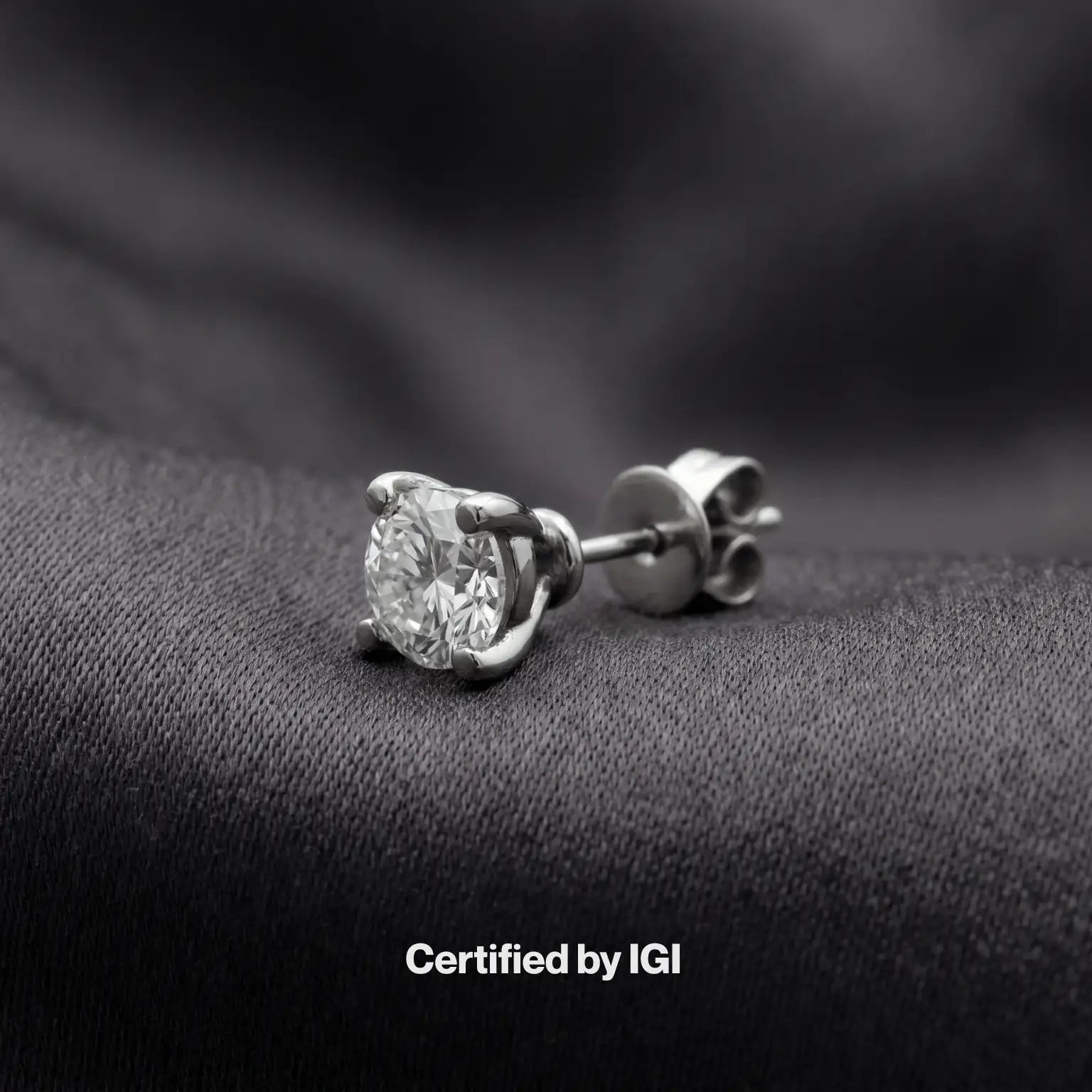 Diamond stud earrings on a dark fabric background with 'Certified by IGI' text.