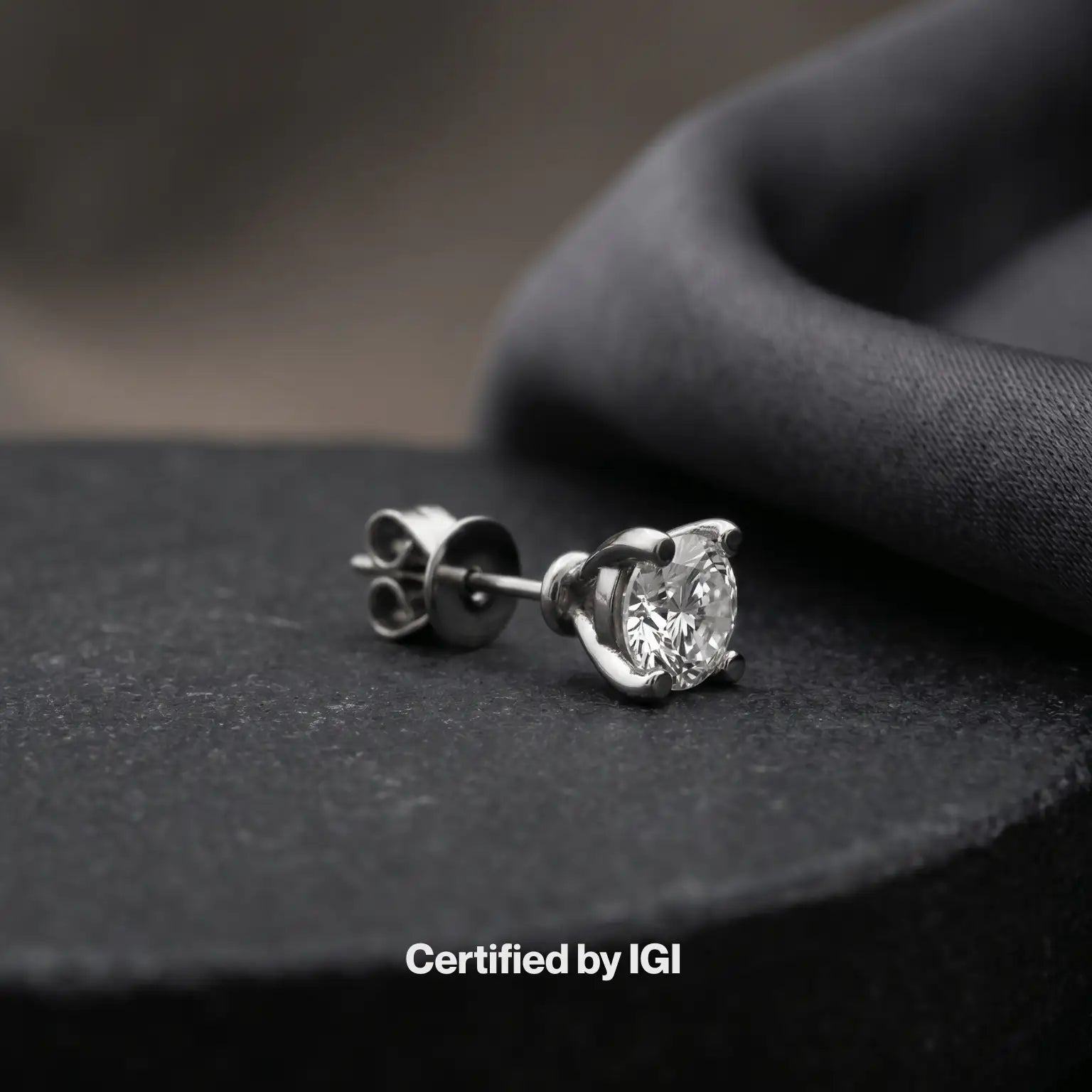 Diamond stud earrings on a dark fabric background with 'Certified by IGI' text.