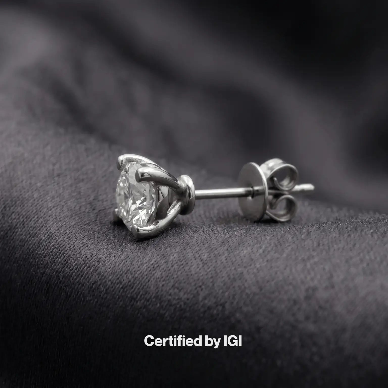 Diamond stud earring on a dark fabric background with 'Certified by IGI' text.