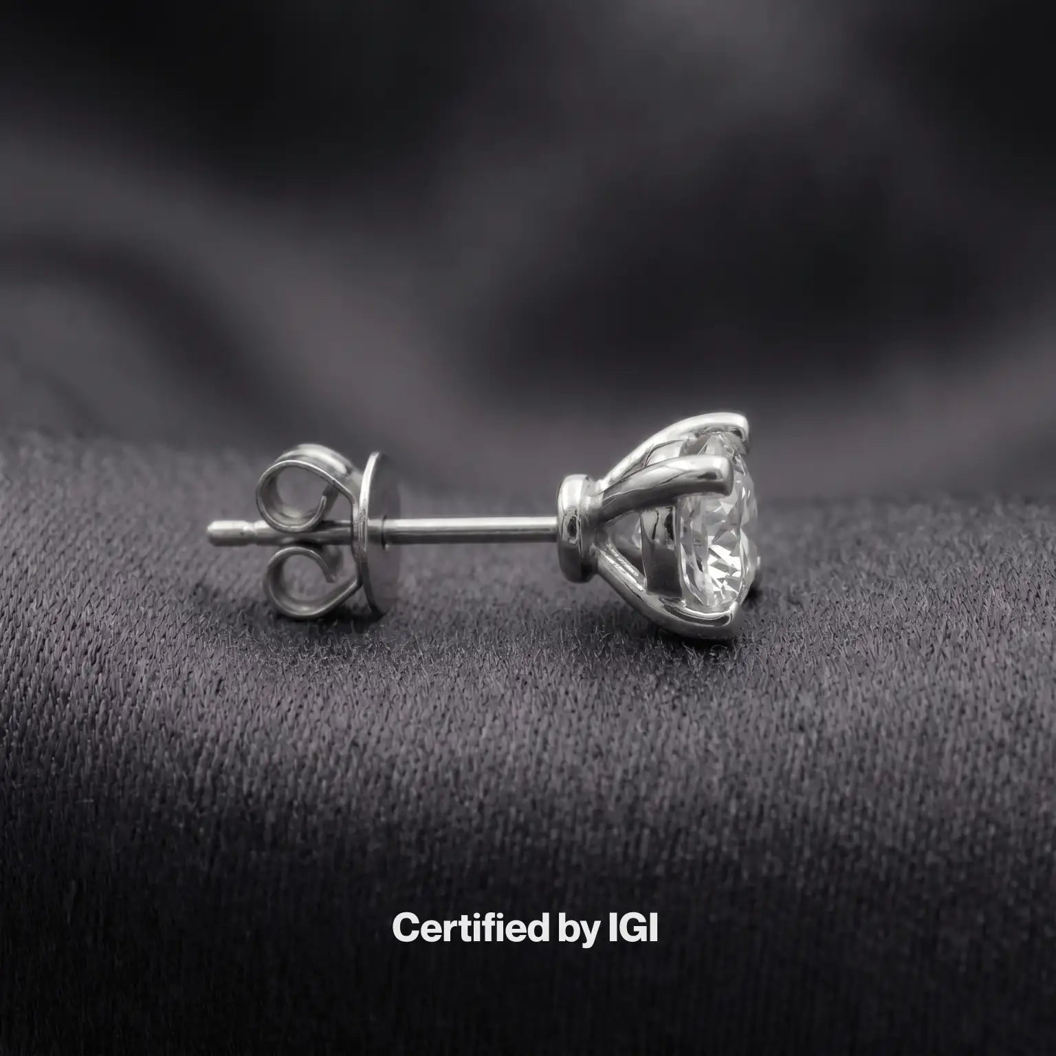 Diamond stud earrings on a dark fabric background with 'Certified by IGI' text.
