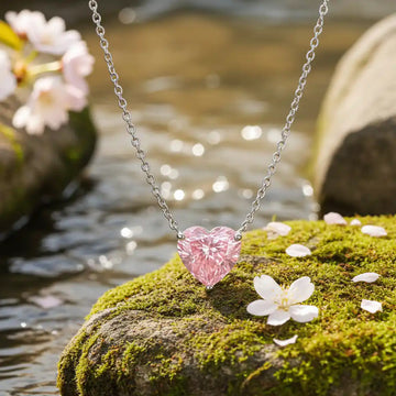 Heart-shaped pink pendant necklace on a mossy rock with cherry blossoms