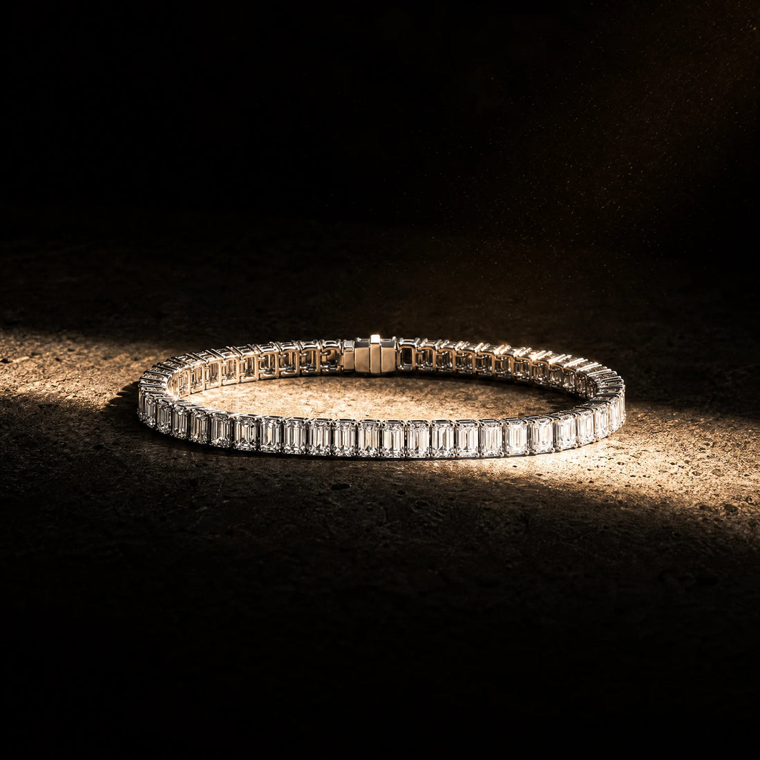 Meridian men's emerald-cut tennis bracelet coiled under warm light, Carat Club Co.